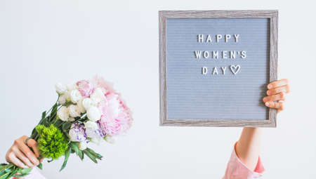Young woman holding pink bouquet and letter board saying happy womens day on gray wall backgroundの写真素材