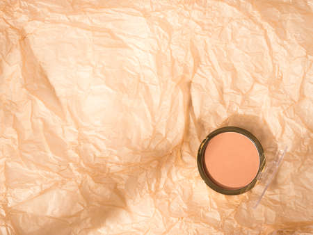 Compact face powder on crumpled neutral beige textured background. Copy space from aboveの写真素材