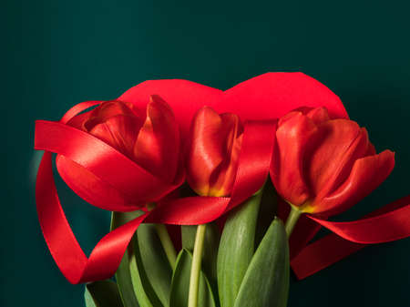 Beautiful red tulips and heart shaped gift box on metallic green background from above. Valentines, womens dayの写真素材