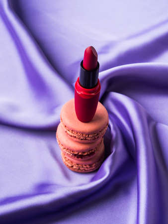 Red lipstick and pink macaroons on purple silk fabric backgroundの写真素材