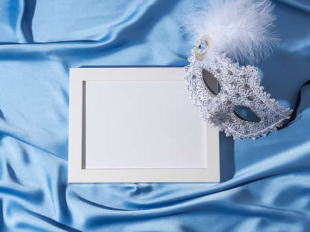 Carnival mask with feather on blue satin background with white frame for text