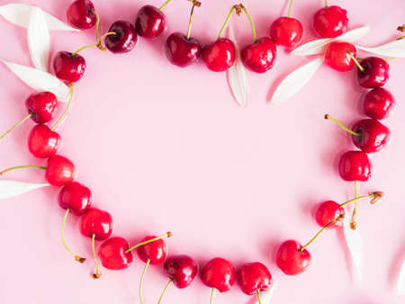 Cherry berry heart shaped frame with petals in water on pink background