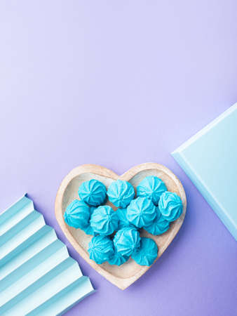 Blue turquoise meringue on heart shaped dish with gift box and decor on pastel purple backgroundの写真素材