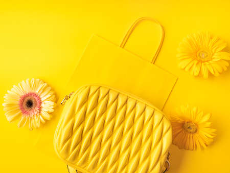 Yellow fashion lady handbag with gerbera flowers on monochrome background with paper shopping bagの写真素材