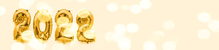 2022 new year numbers in golden foil balloons on beige background, web banner with festive bokehの写真素材