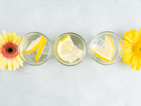 Lemon water drink with ice cubes on stone background with gerbera daisy yellow flowers