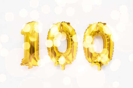 Number 100 one hundred golden foil balloon party decor on white background, birthday anniversary