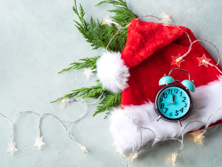 Santa Claus cap with fir tree branches, star lights and retro clock on turquoise gray background