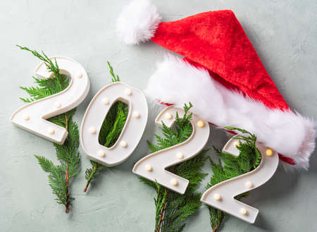 New year 2022 numbers with fir tree branches and santa cap on gray background. Holiday greeting card