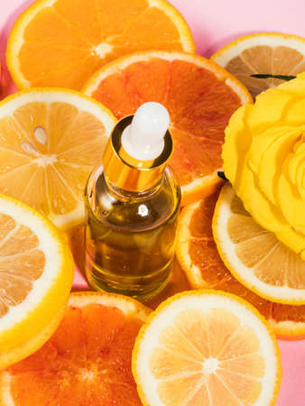 Vitamin C serum bottle with dropper on pink background with orange citrus slices