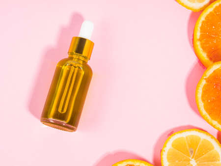 Vitamin C serum bottle with dropper on pink background with orange citrus slicesの写真素材