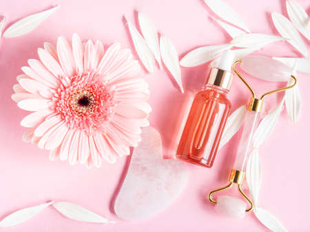 Cosmetic beauty serum oil acid bottle product and quartz face roller guasha on pink backgroundの写真素材