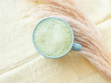 Matcha tea latte morning antioxidant hot drink in blue cup on yellow table cloth with pampas grassの写真素材