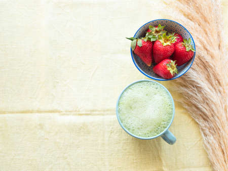 Matcha tea latte morning antioxidant hot drink in blue cup on yellow table cloth with pampas grass