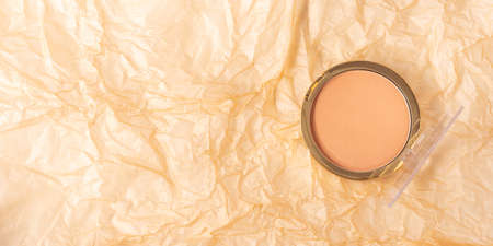 Compact face powder on crumpled beige textured background