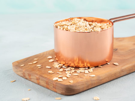 Rolled oats in measuring cup on wooden boardの写真素材