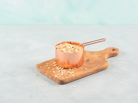 Rolled oats in measuring cup on wooden boardの写真素材