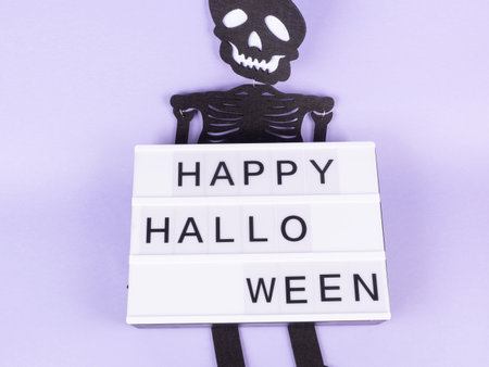 Happy halloween greetings on lightbox with skeleton on purple background