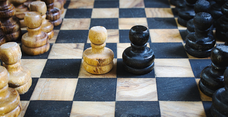 Old olive wood chess set board with staunton pieces and black and white pawns battling head-to-head