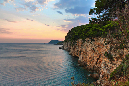 Cliff face with the sea and a beautiful sunset with birds flying in the sky - island of Kolocep in Croatiaの写真素材