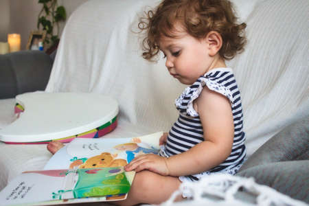 Little baby girl reading a picture book on a white sofaの写真素材
