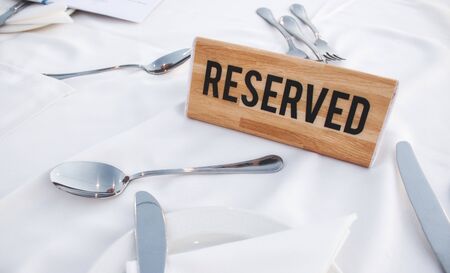 A wooden Reserved sign on a restaurant table with a white tablecloth and shiny cutleryの写真素材