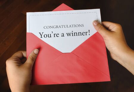 An open red envelope with a letter that says Congratulations You're a winner! with female hands...