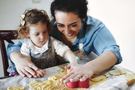 Mother and daughter baking cookies in the kitchen - cutting pastry dough with plastic shape cuttersの写真素材