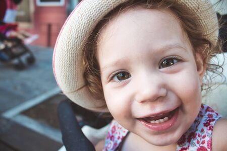 Close-up portrait of cute baby girl looking at camera smiling and wearing a hatの写真素材