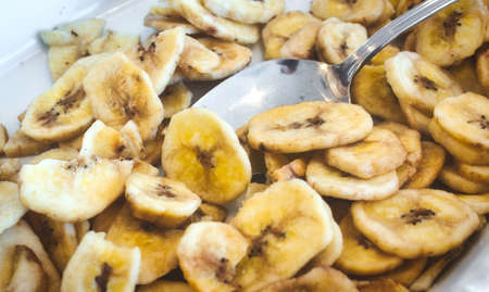 Banana chips in a white breakfast bowl with a spoonの写真素材