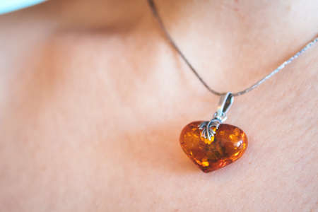A heart shaped amber pendant worn around the neck of a young womanの写真素材