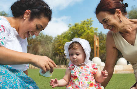 A happy family of 3 generations, baby, mother and grandmother sitting on the grass and playing...