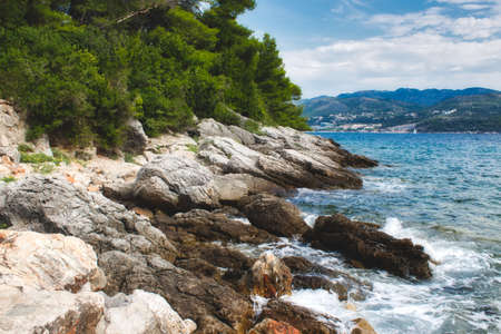 Rocks on the water's edge with a green forest and hills on an island in the backgroundの写真素材