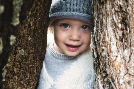 Close up of beautiful young girl model smiling and peering through a gap between tree trunks in the...