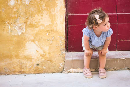 Cute baby girl sitting on the doorstep of a rural village homeの写真素材