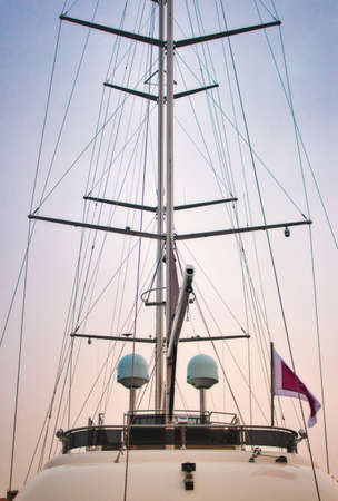 Mast of a luxury sailing yacht with sails down showing the rigging against a multi-colored skyの写真素材