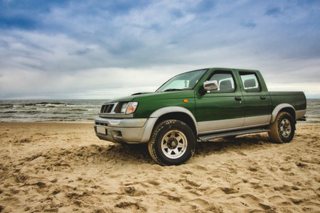 Green pick-up truck parked on the sandy beach with sea, blue sky and clouds in the backgroundの写真素材
