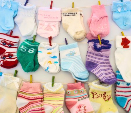 Baby socks and mittens hanging on lines with miniature clothes pegsの写真素材