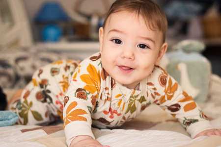 Cute baby on a bed wearing a romper suit pajama looking directly at the cameraの写真素材