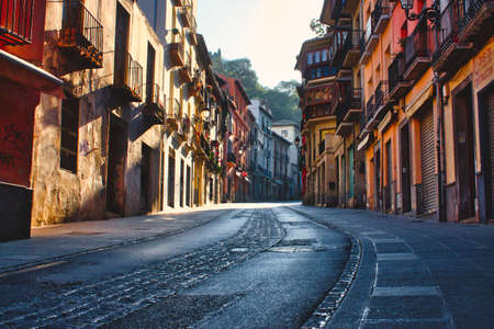 A moody and picturesque view of a street in Granada, Spain, winding uphill with tall buildings on either sideの写真素材