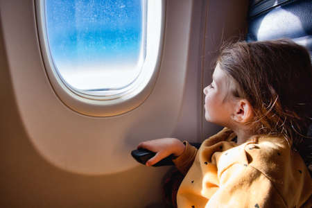 Little girl sat on a commercial flight airplane looking out of the windowの写真素材