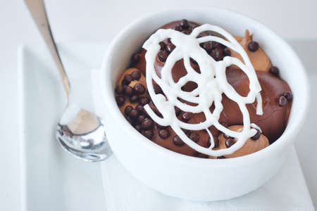 Profiteroles with a white chocolate lattice topping in a white ceramic bowl with silver spoon