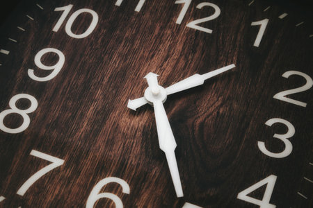 Close-up of an wooden analogue clock face with white numbers and hour and minute hand showing the timeの写真素材