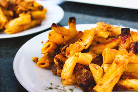 Penne pasta tubes with bolognese sauce on a white plate on a kitchen worktopの写真素材