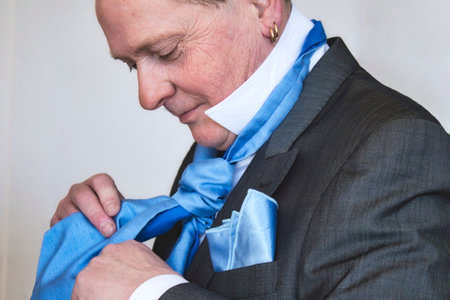 A middle-aged man putting on a silk blue tie dressed in a suit getting ready for a weddingの写真素材