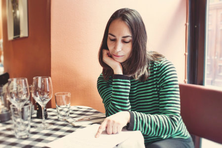 One attractive young lady sat at a table reading the menu in a bistro restaurant on her ownの写真素材