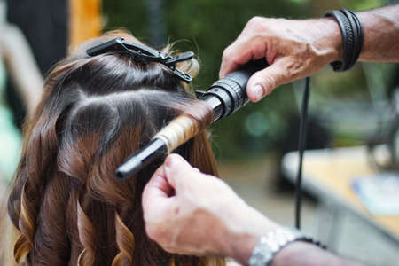 Back of the head of a young woman having her hair curled by a stylist using a curling ironの写真素材