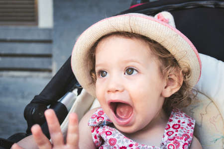 A cute white Caucasian little girl wearing a round straw summer hat looking surprised and happyの写真素材