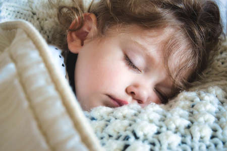 Close-up of a little girl sleeping peacefully wrapped up in a warm blanketの写真素材