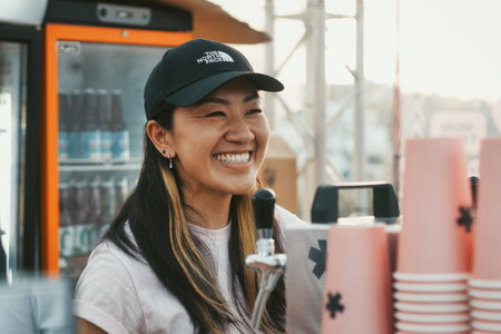 A cute smiley Asian girl working behind the counter at an open-air bar selling beer